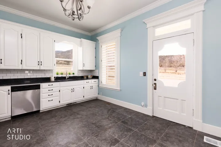 Kitchen with stainless steel dishwasher, white cabinets, ornamental molding, hanging lights, and tasteful backsplash