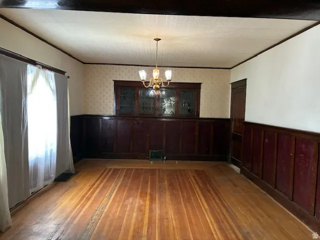 Unfurnished dining area featuring wainscoting, ornamental molding, light wood-type flooring, suspended lighting, and wallpapered walls