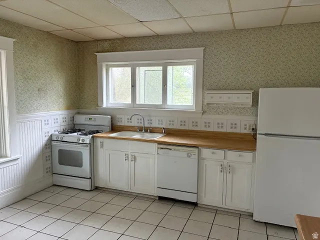 Kitchen with wallpapered walls, white appliances, a drop ceiling, white cabinetry, and light countertops