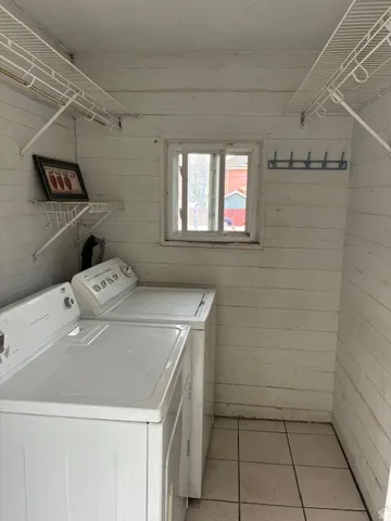 Laundry room featuring wooden walls, washing machine and clothes dryer, light tile patterned flooring, and a barn door