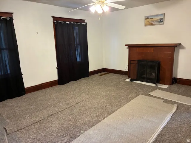 Unfurnished living room with carpet, ceiling fan, and a tile fireplace