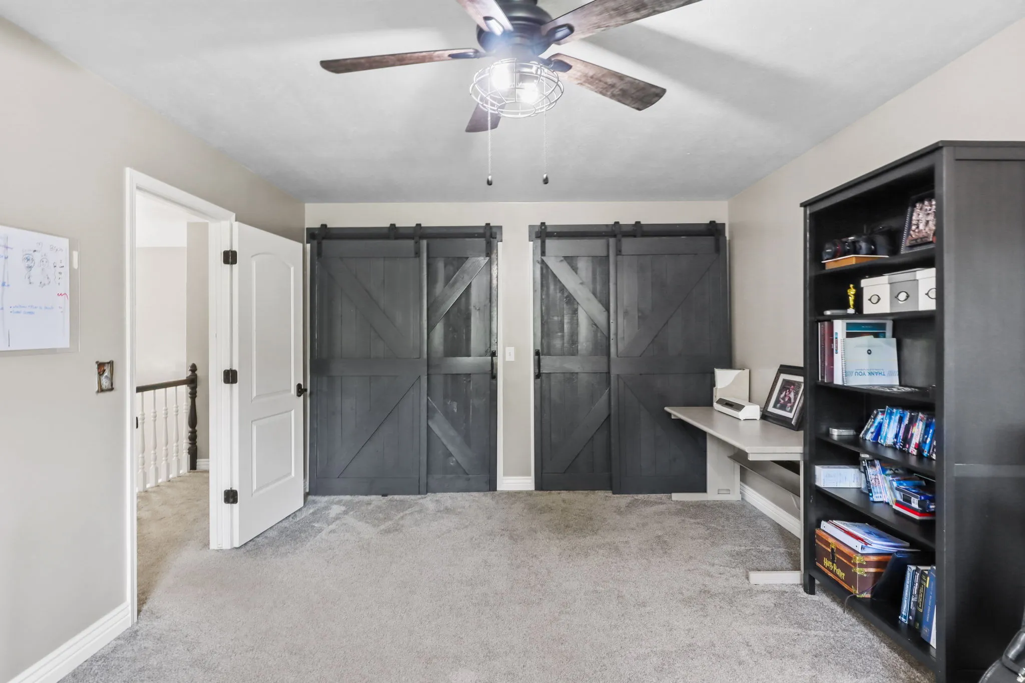 Office with a barn door, ceiling fan, and light colored carpet