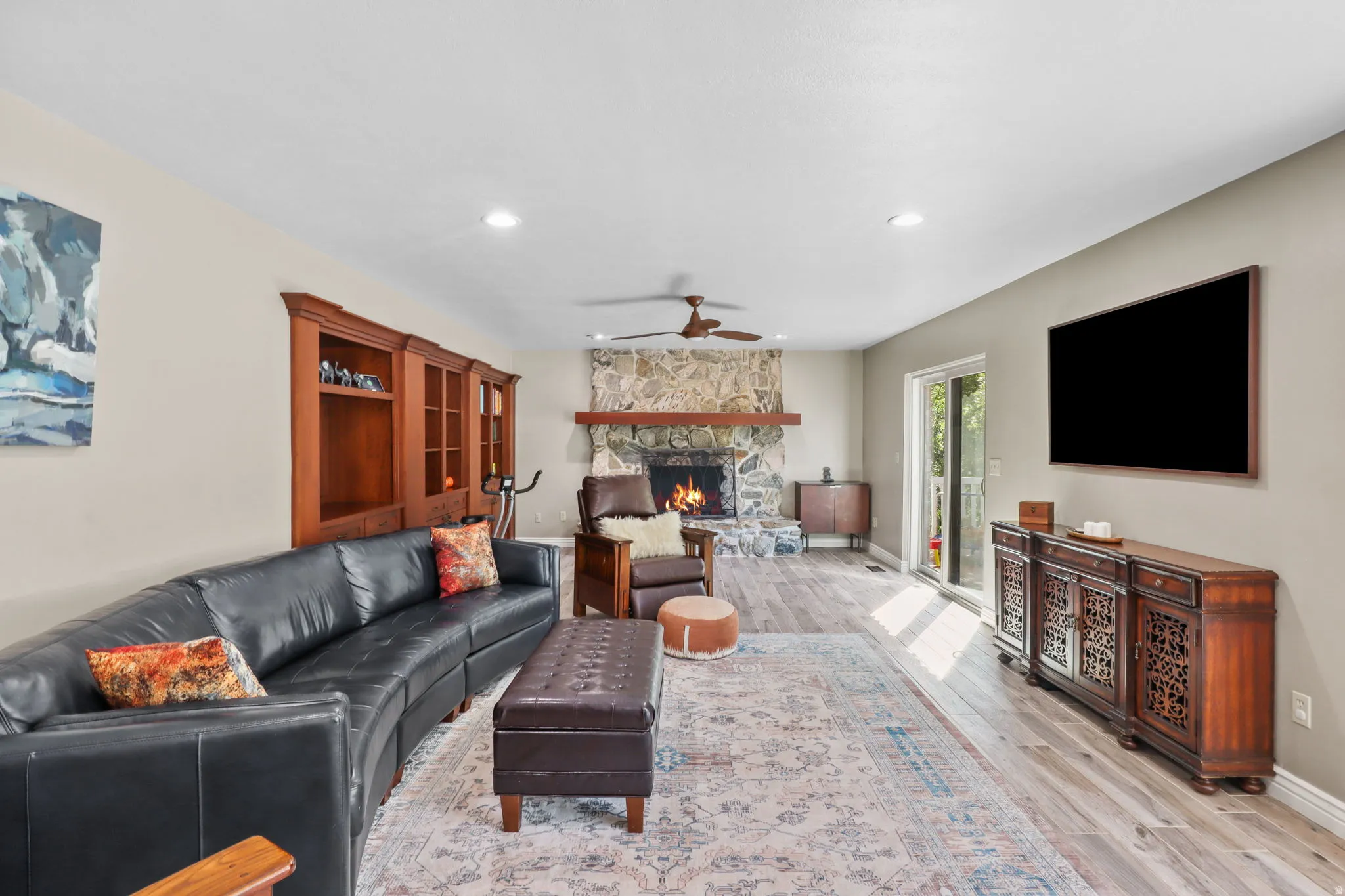 Living room featuring a stone fireplace, ceiling fan, light wood-style flooring, and recessed lighting