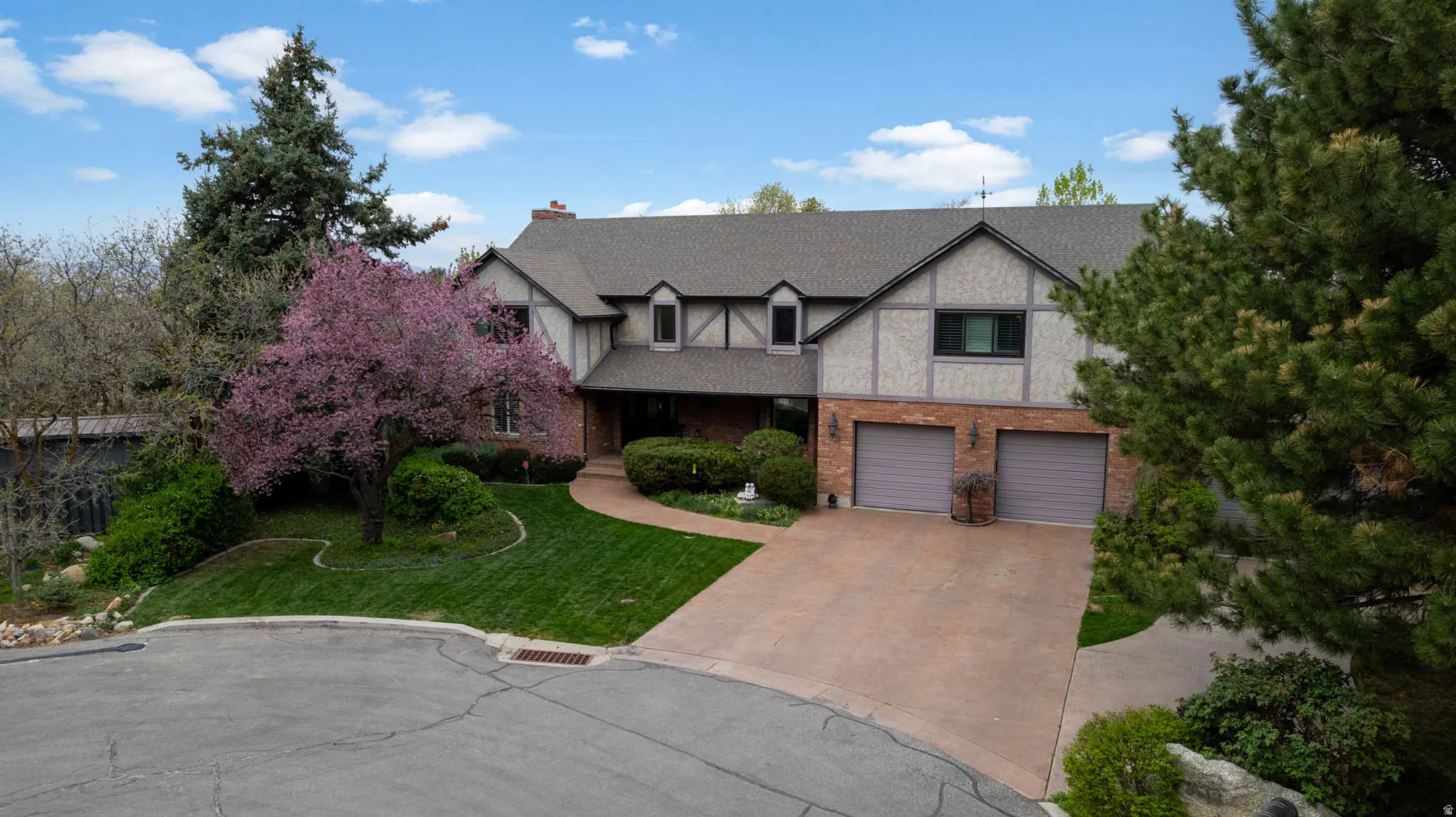 Tudor home with a front yard, brick siding, driveway, a garage, and a chimney