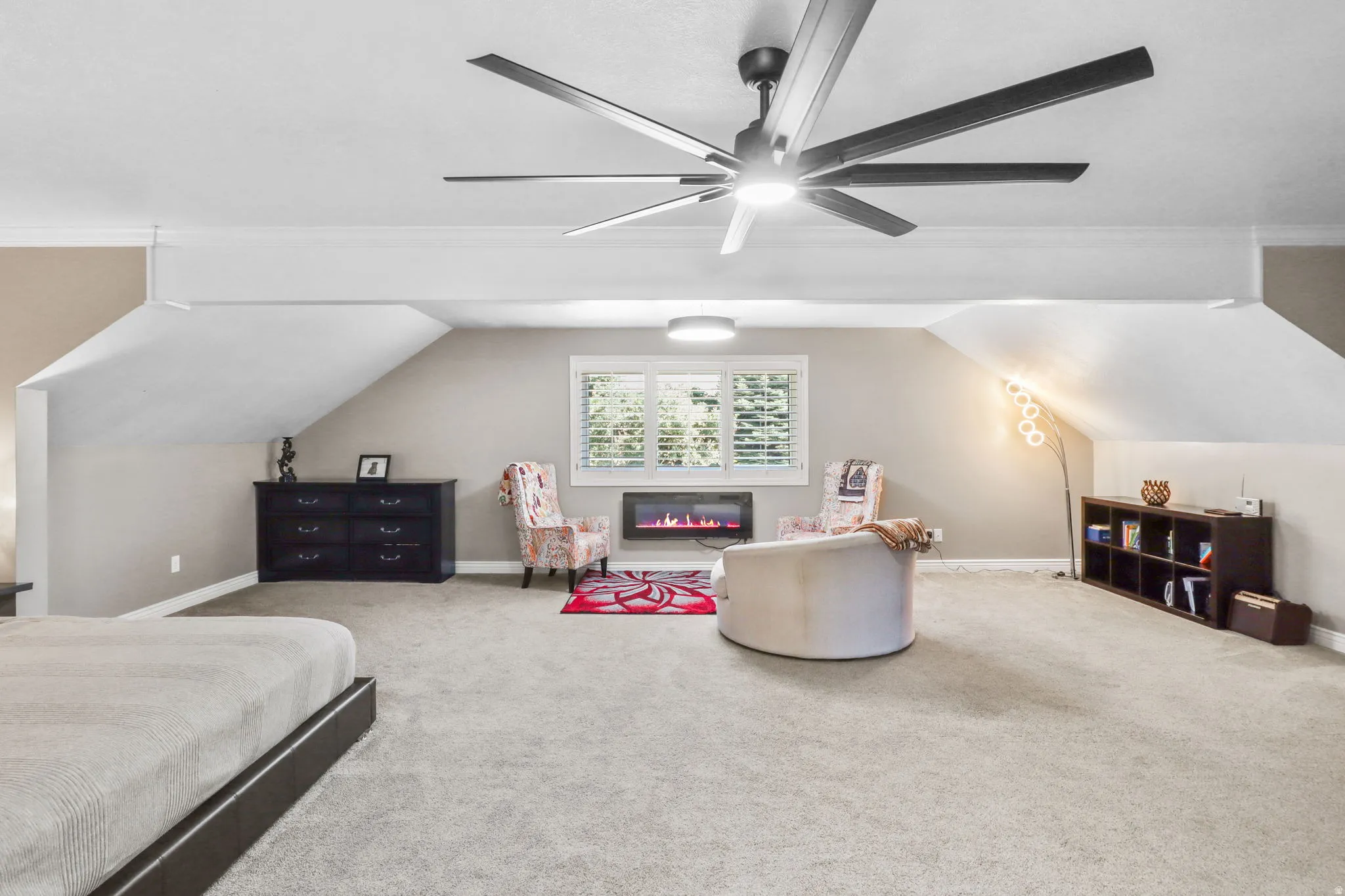 Bedroom with carpet flooring, a glass covered fireplace, ceiling fan, and vaulted ceiling