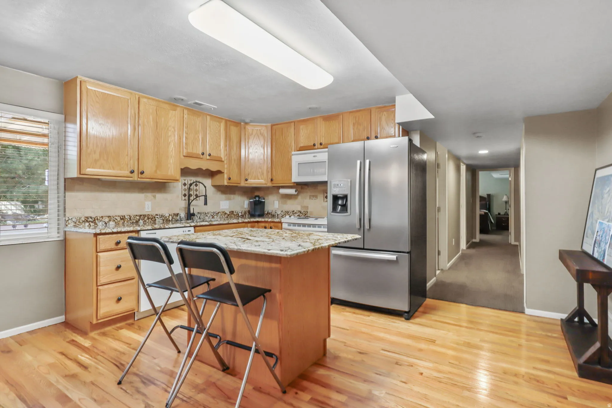 Kitchen featuring light stone counters, white appliances, a kitchen island, and backsplash
