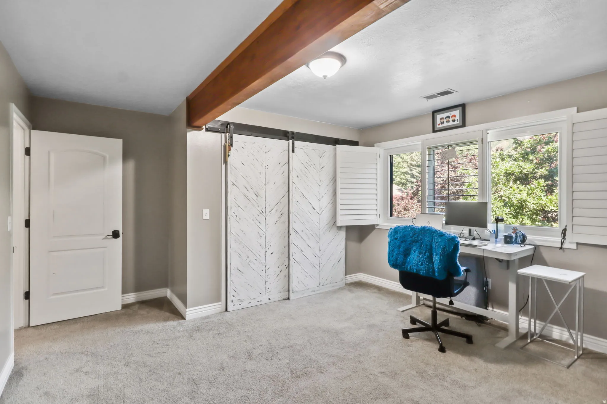Home office featuring a barn door, light carpet, and beam ceiling