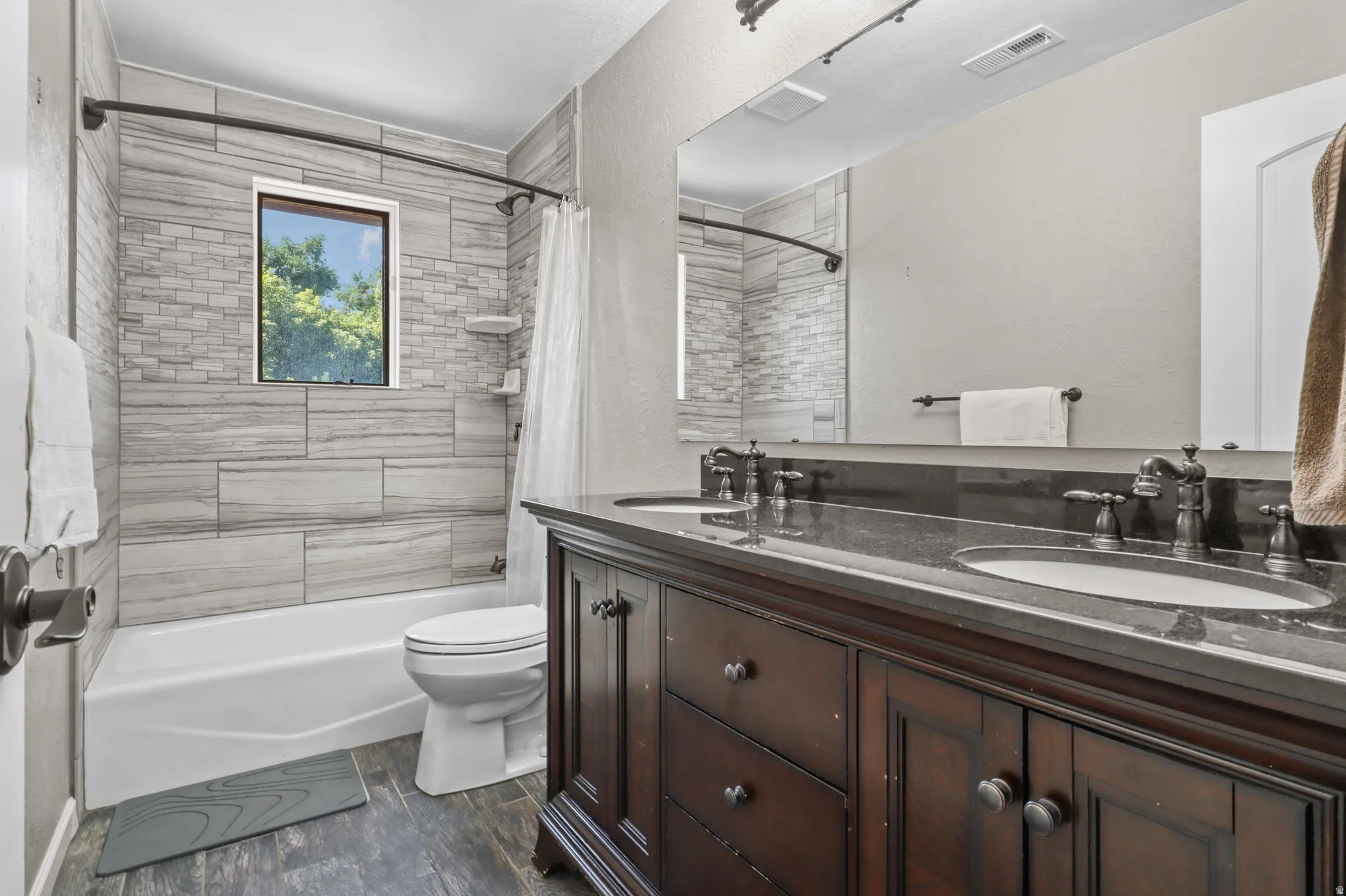 Full bathroom featuring double vanity, shower / bath combo, and dark wood-type flooring