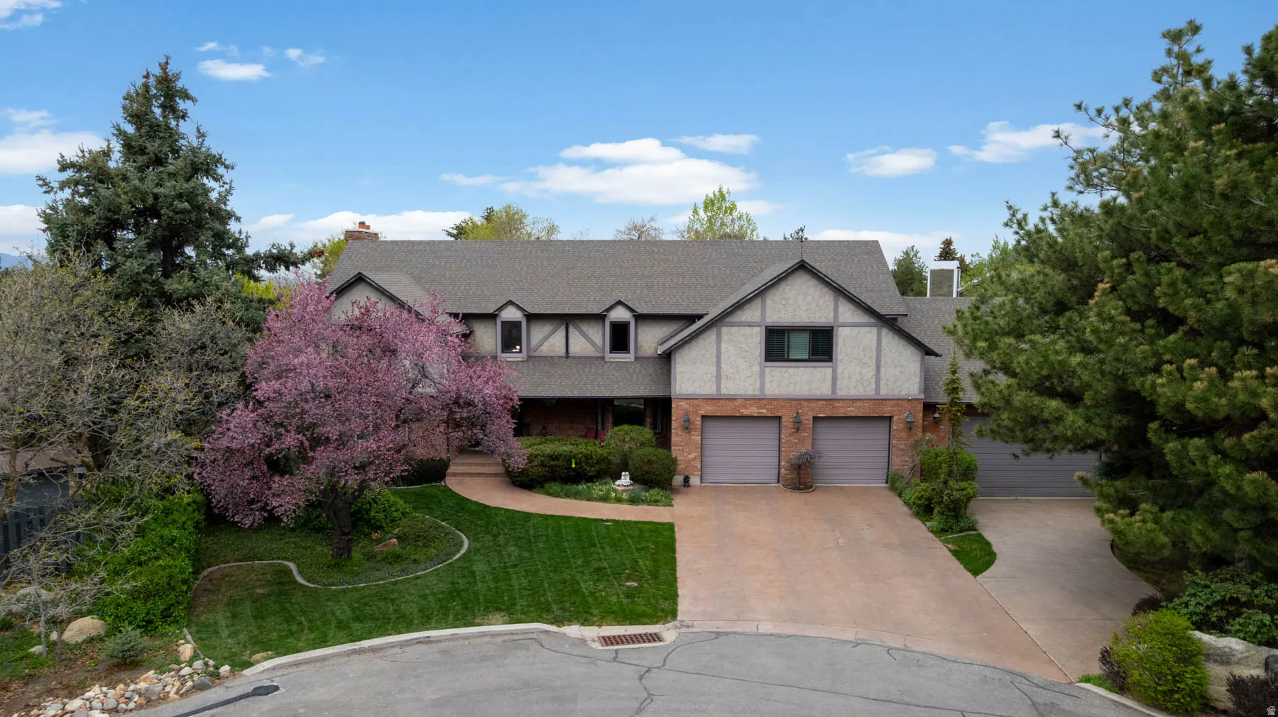 Tudor-style house featuring a chimney, a front yard, driveway, and brick siding