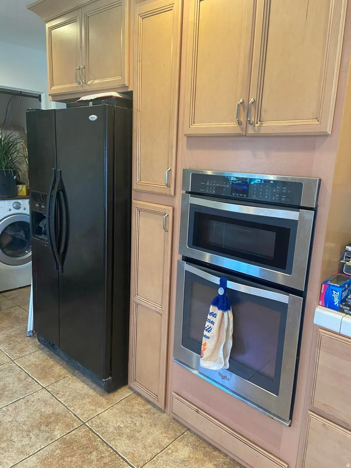 Kitchen with double oven, black refrigerator with ice dispenser, washer / clothes dryer, and light tile patterned floors