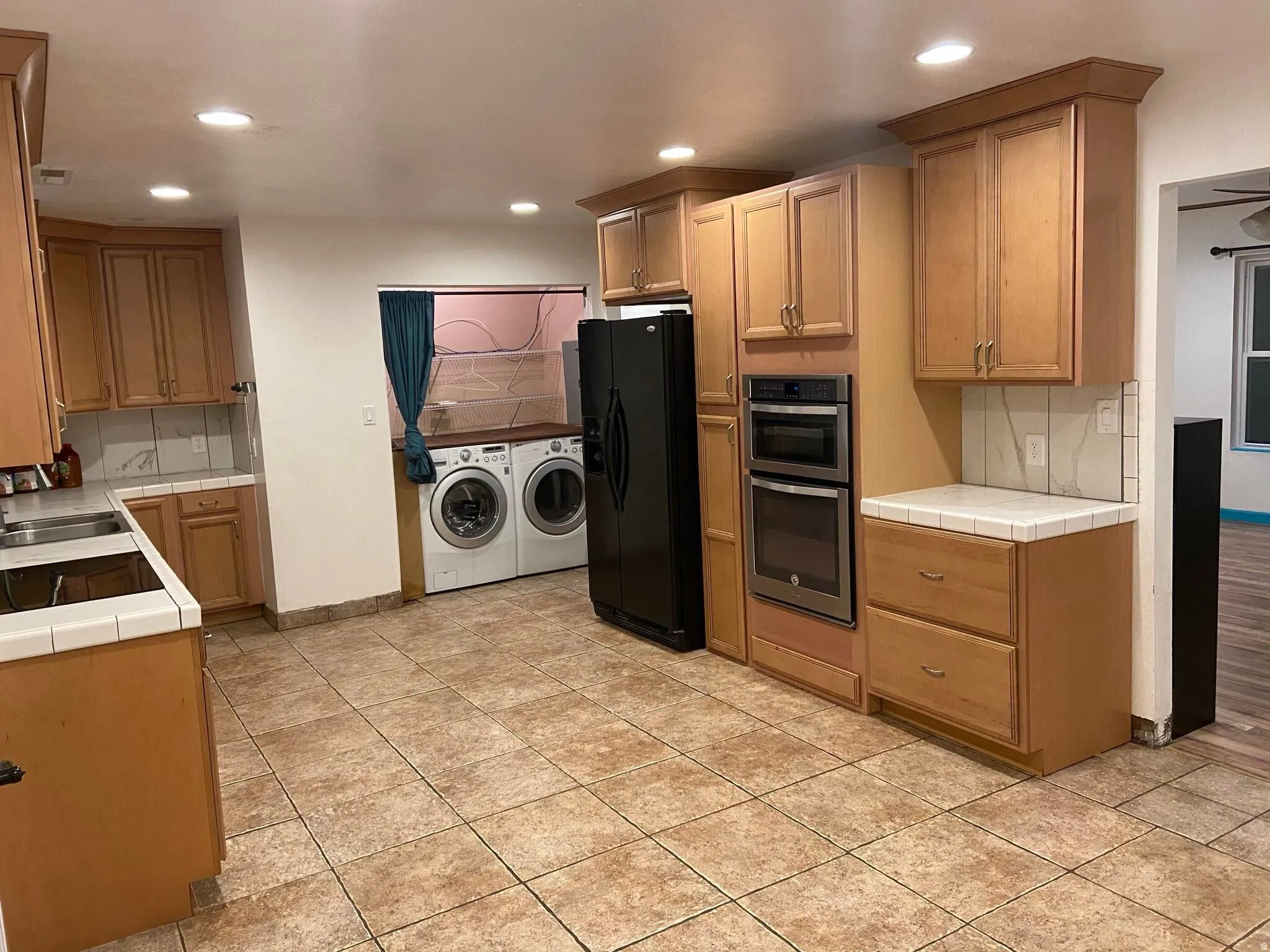 Kitchen with tasteful backsplash, tile counters, washing machine and clothes dryer, black refrigerator with ice dispenser, and recessed lighting