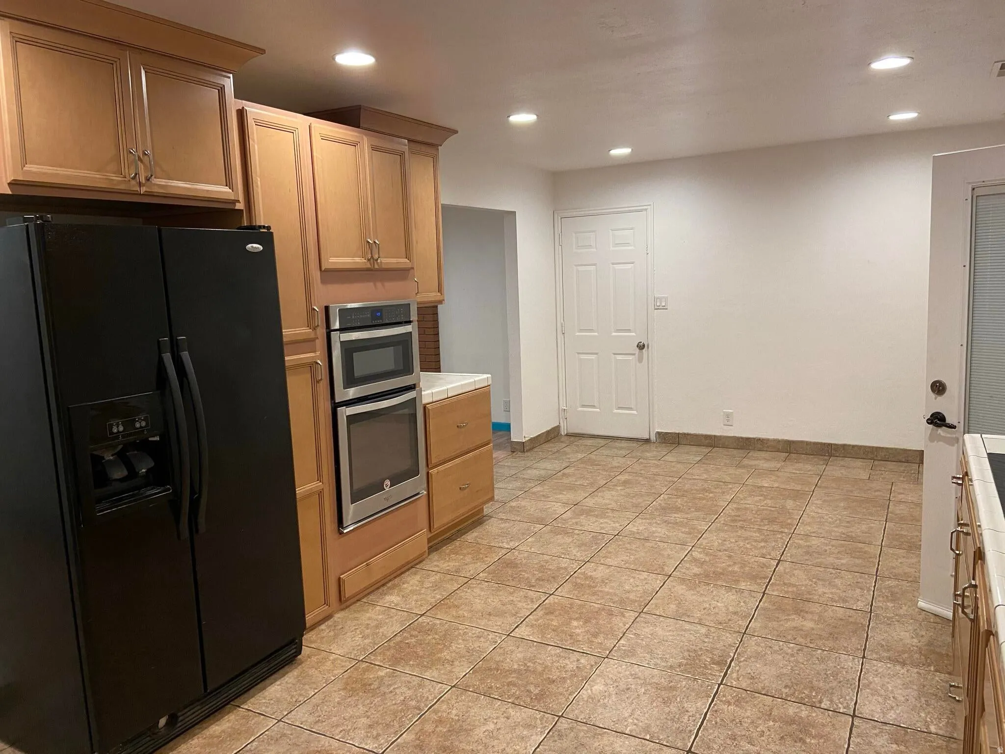 Kitchen with black fridge, recessed lighting, stainless steel double oven, light tile patterned floors, and light wood finish cabinetry