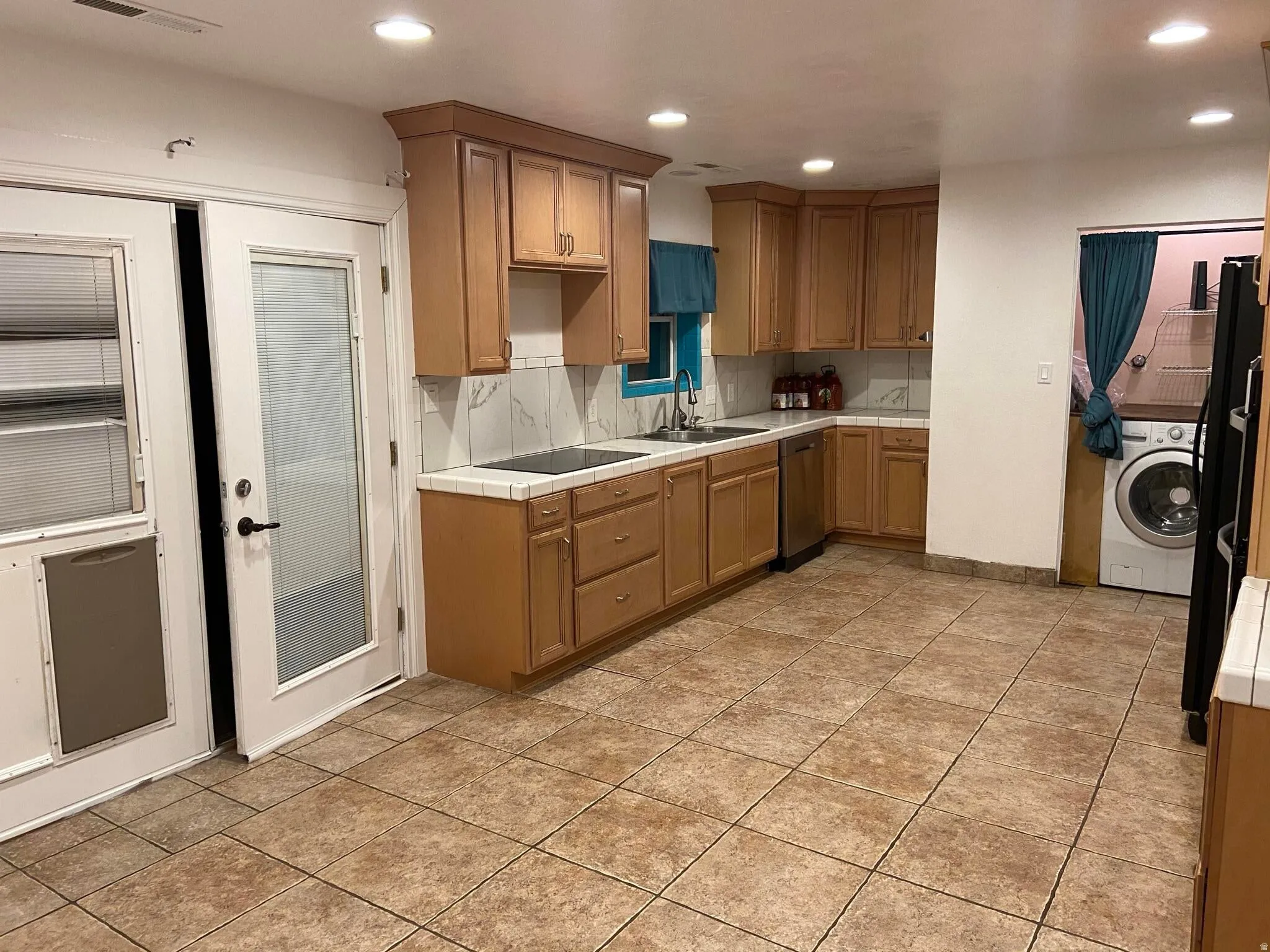 Kitchen featuring tile counters, recessed lighting, black appliances, washer / dryer, and tasteful backsplash