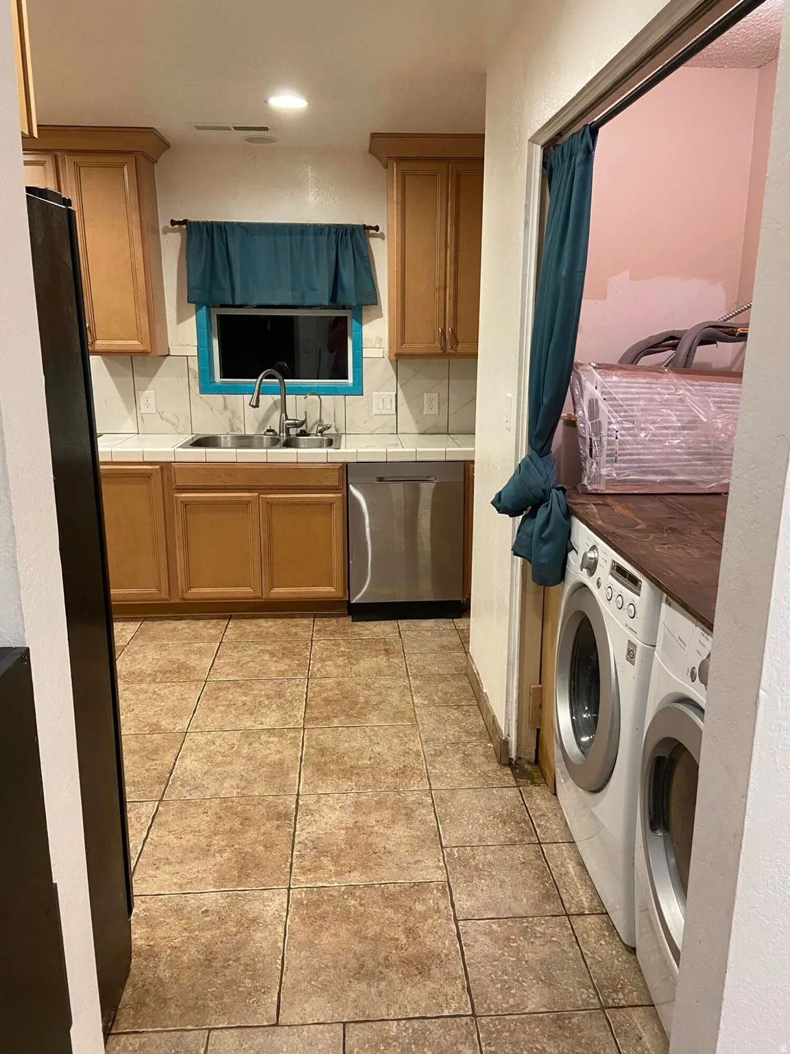 Kitchen with separate washer and dryer, dishwasher, light tile patterned floors, tile counters, and decorative backsplash