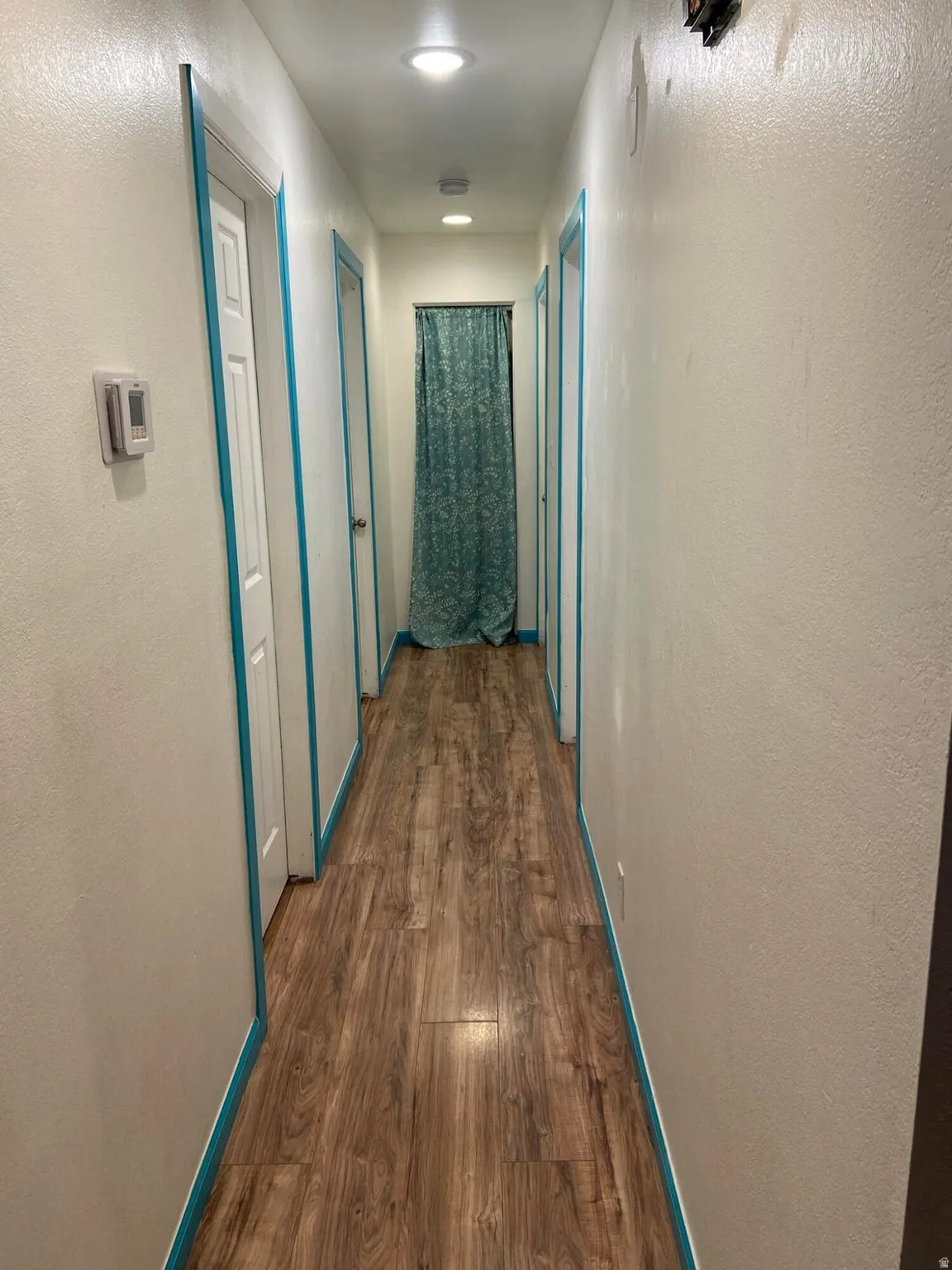 Corridor featuring a textured wall and dark wood-style flooring