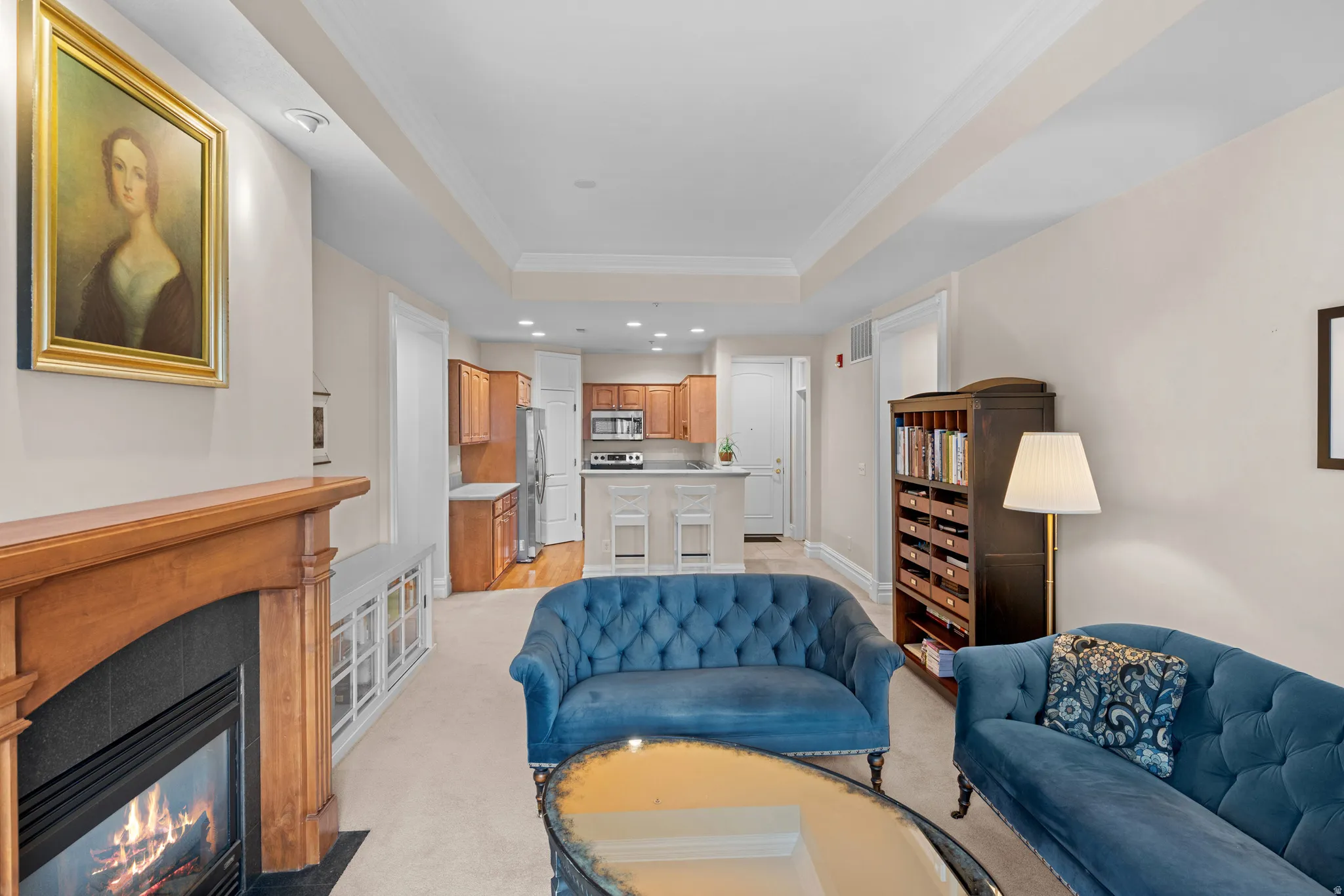 Living area featuring crown molding, a raised ceiling, recessed lighting, light carpet, and a fireplace with flush hearth