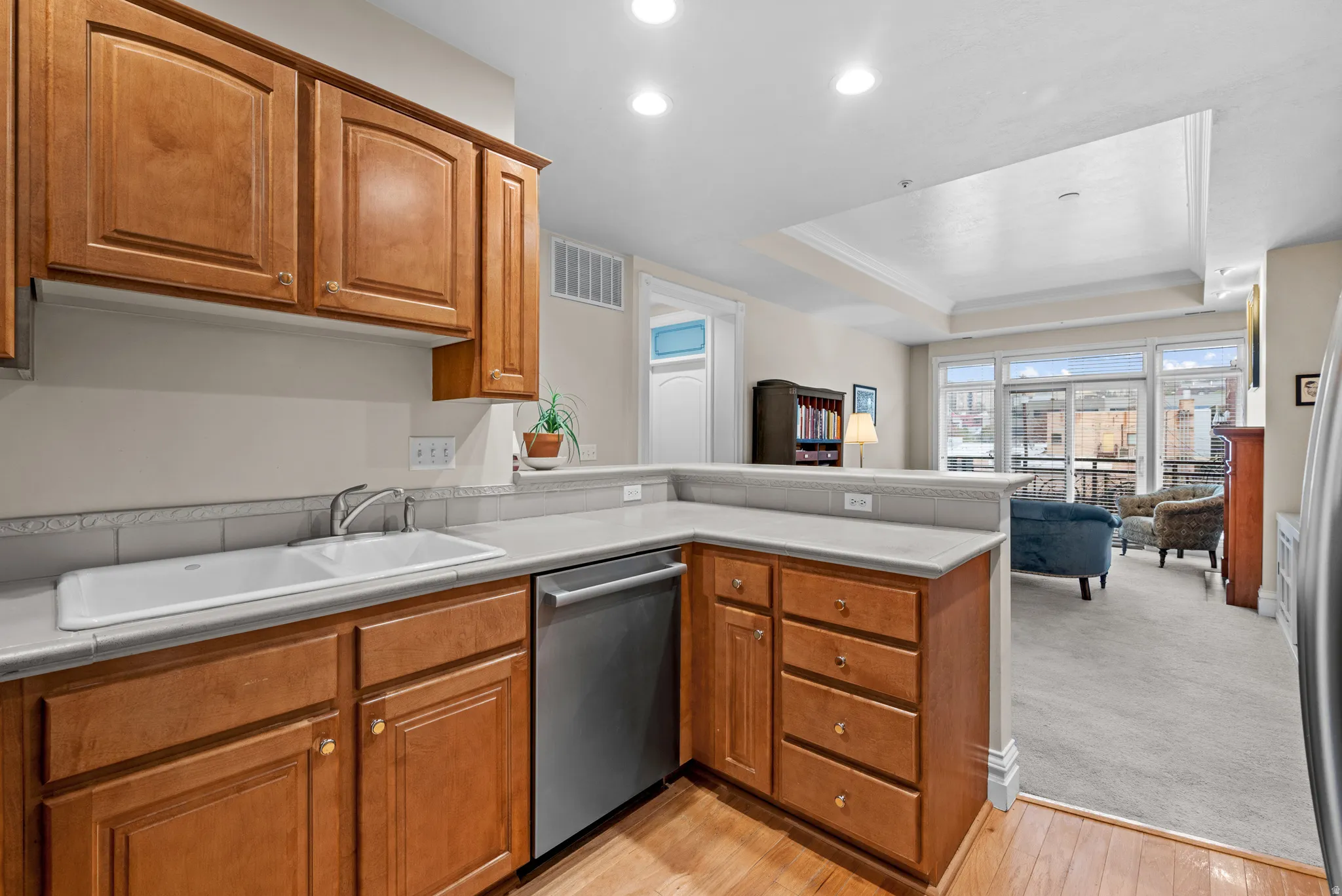 Kitchen featuring a peninsula, wood finish cabinetry, light countertops, dishwasher, and open floor plan