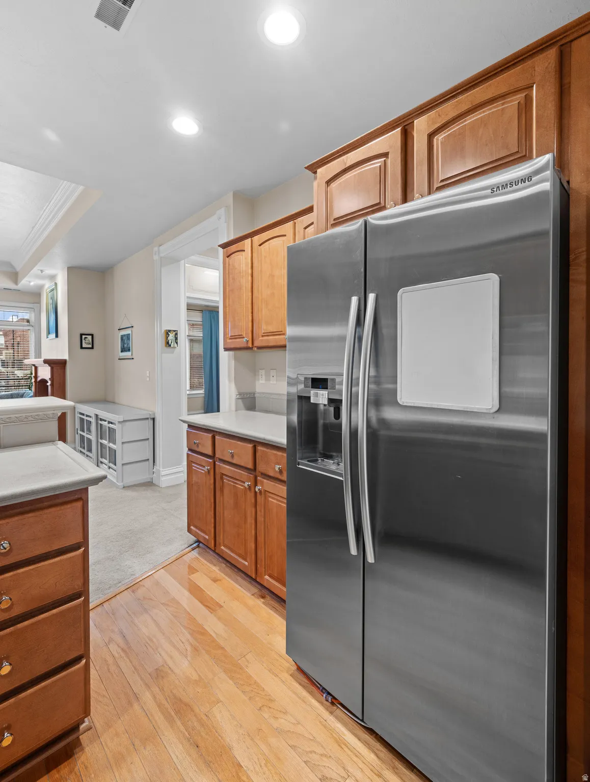 Kitchen with stainless steel refrigerator with ice dispenser, light countertops, light wood finished floors, recessed lighting, and wood finish cabinetry