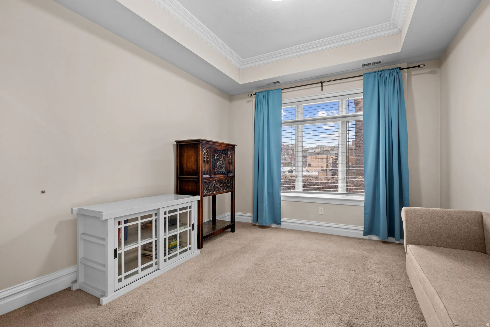 Sitting room featuring a tray ceiling, light colored carpet, and ornamental molding