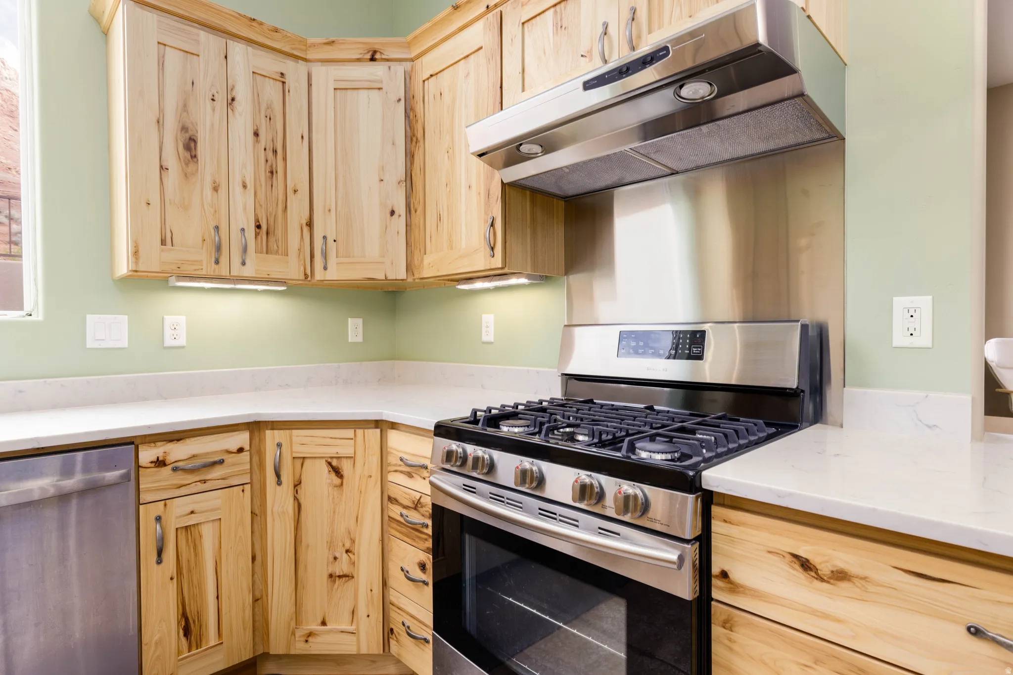 Kitchen with stainless steel appliances, light wood finish cabinets, and light stone countertops