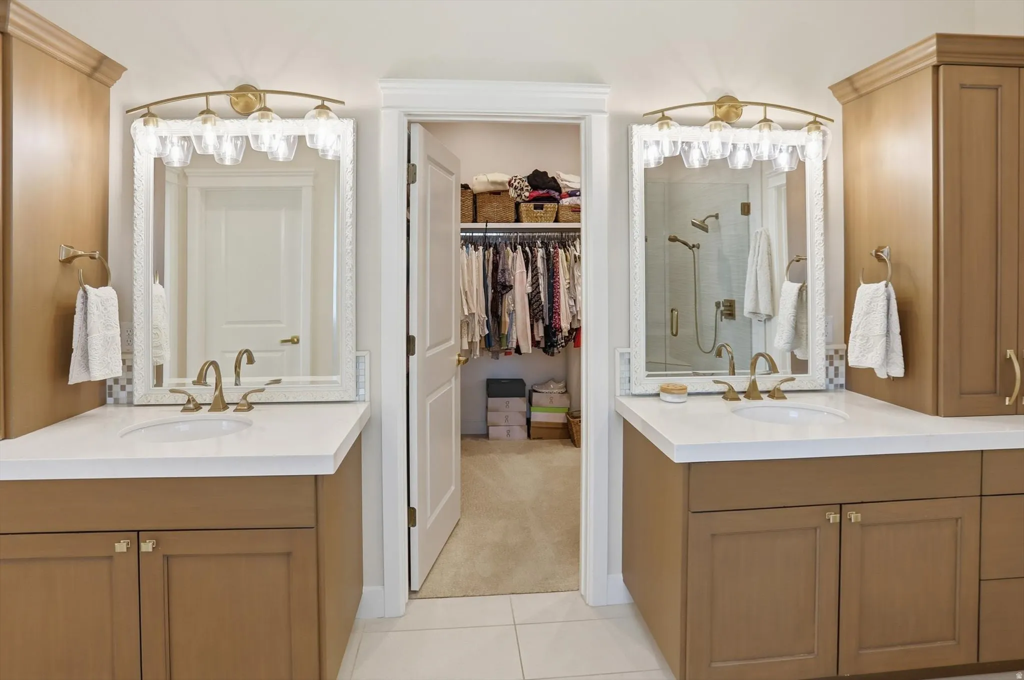Full bath featuring two vanities, a spacious closet, a stall shower, and light tile patterned floors