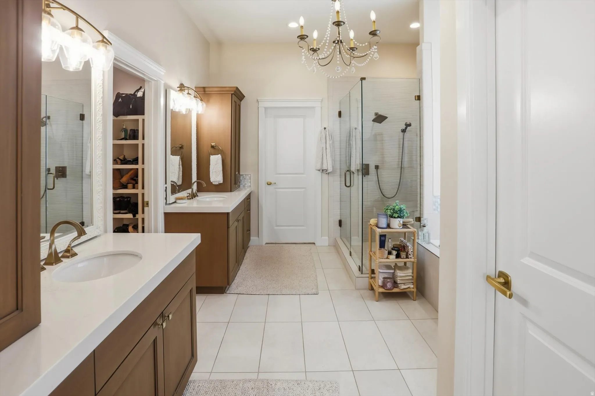 Full bathroom featuring a chandelier, a stall shower, two vanities, and light tile patterned floors