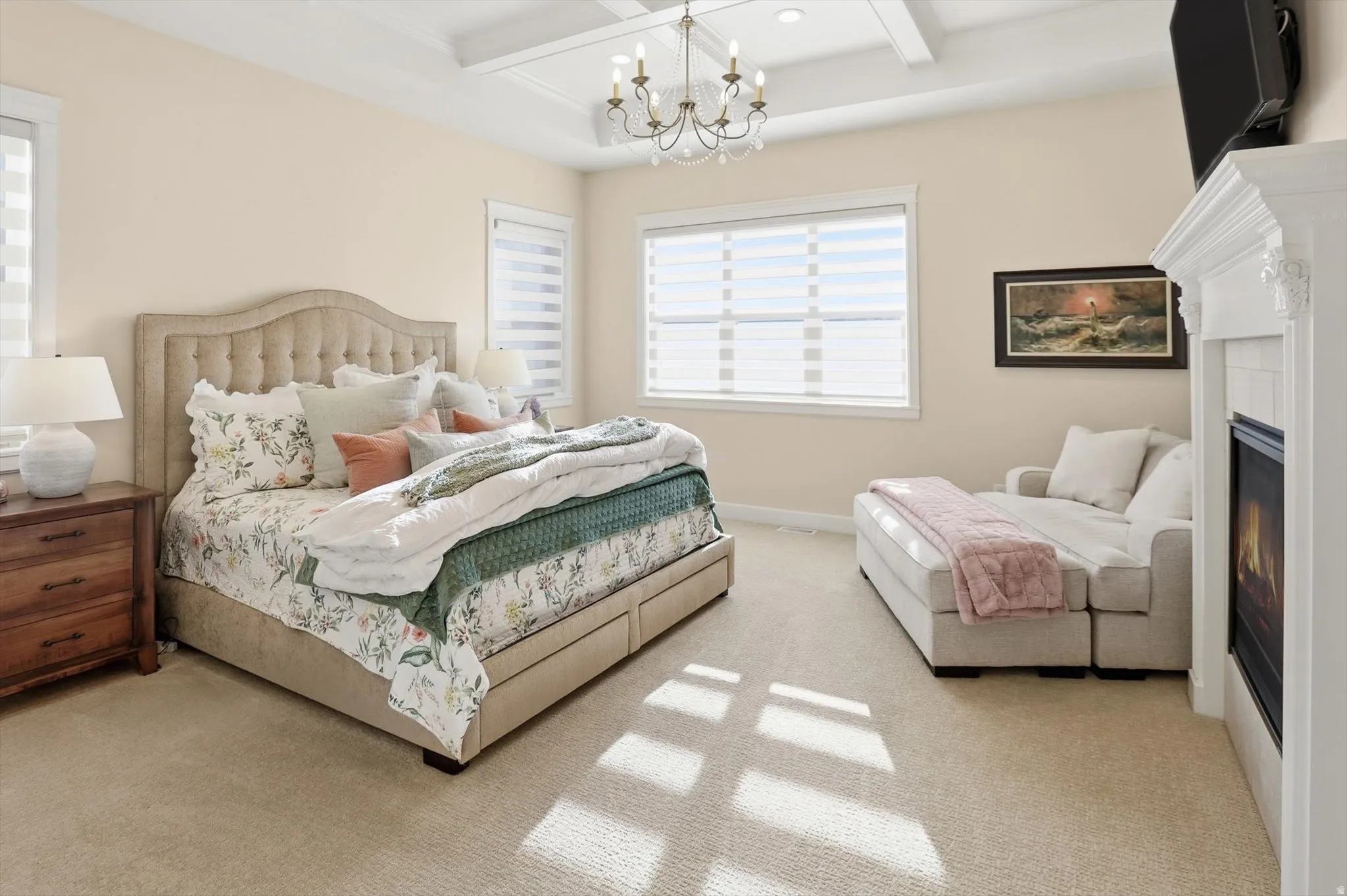 Bedroom with coffered ceiling, a glass covered fireplace, hanging lights, and light carpet