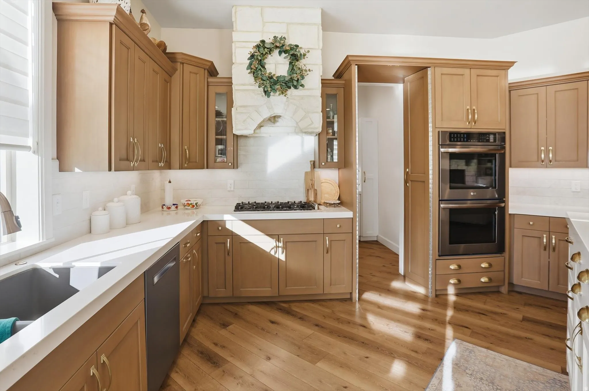 Kitchen with light wood-style flooring, stainless steel appliances, backsplash, glass insert cabinets, and light stone countertops