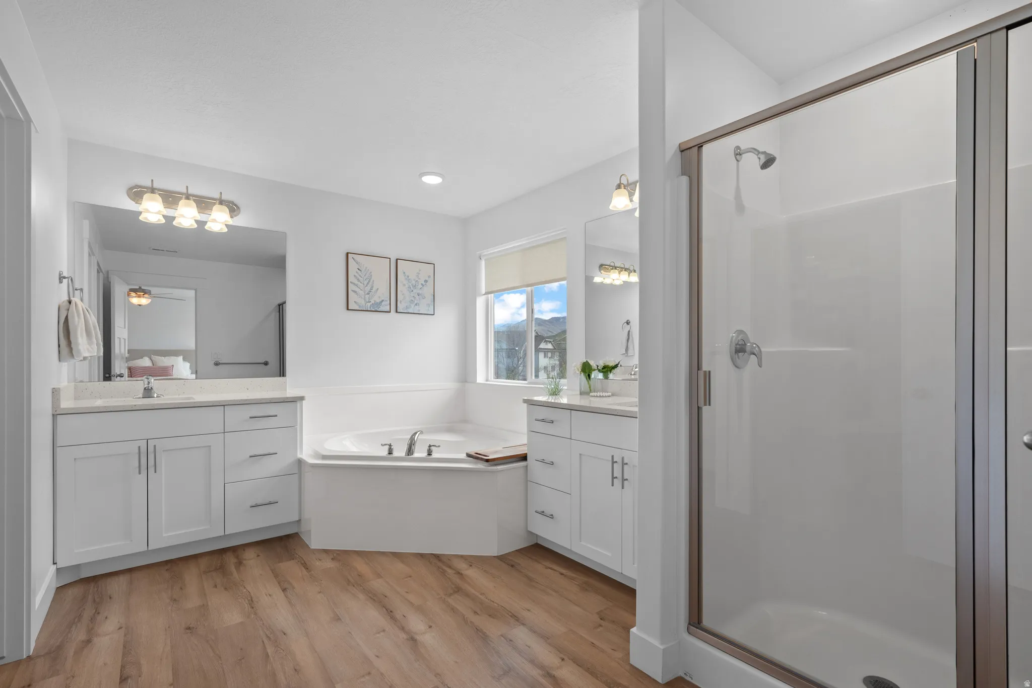 Full bath featuring light wood-style flooring, a stall shower, a garden tub, and two vanities