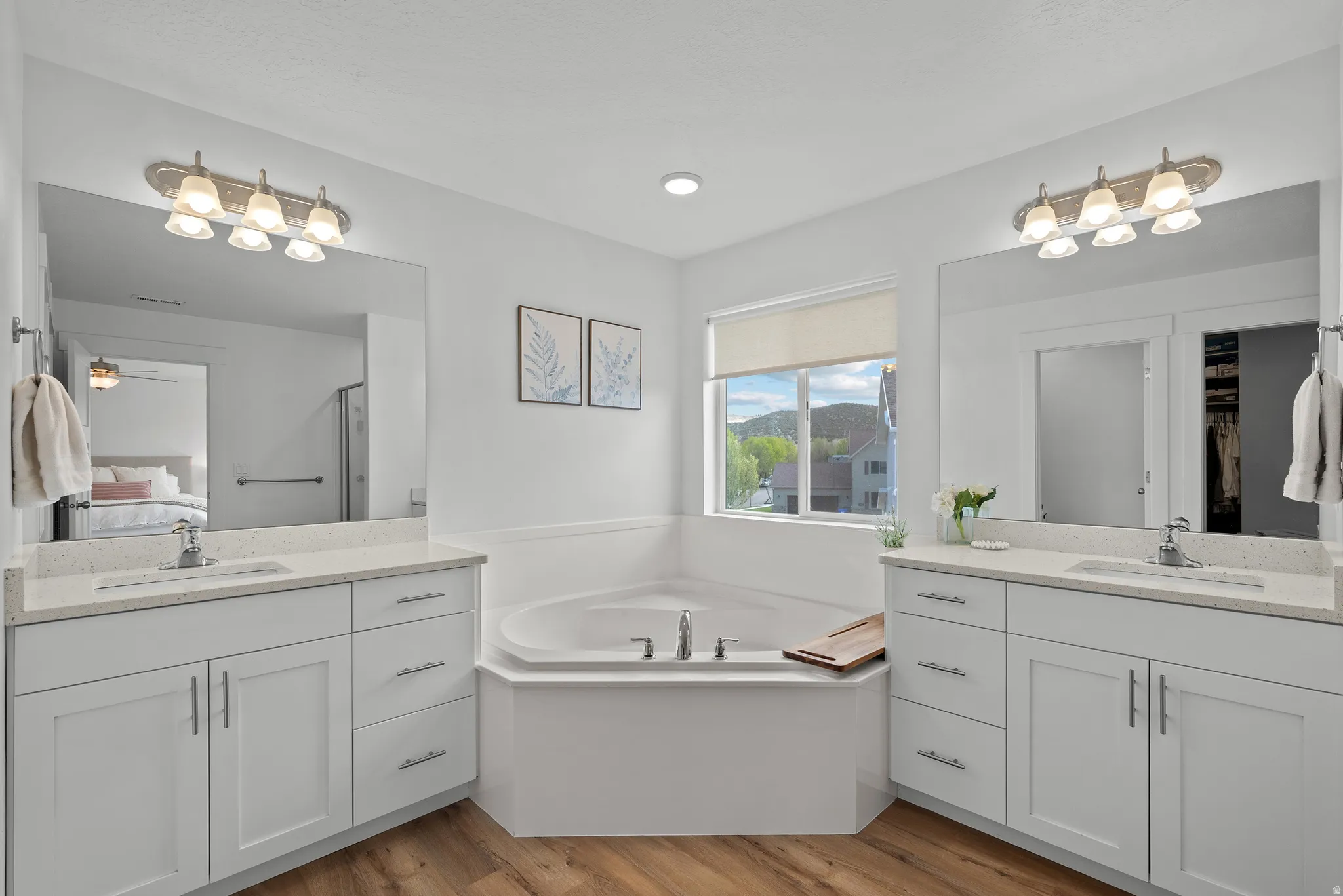 Full bathroom featuring ensuite bathroom, a garden tub, light wood-style flooring, two vanities, and a spacious closet