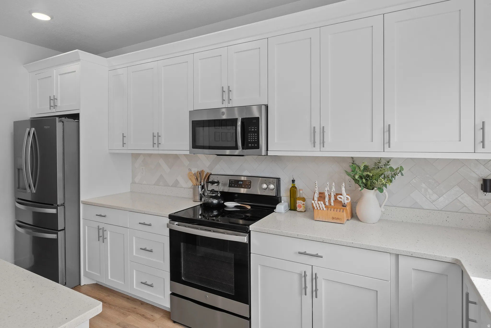 Kitchen featuring stainless steel appliances, light stone countertops, white cabinets, light wood-type flooring, and backsplash