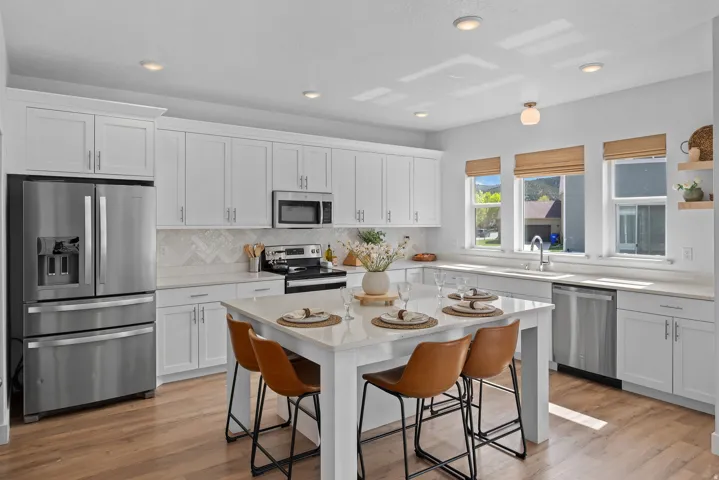Kitchen with stainless steel appliances, white cabinetry, a kitchen bar, light stone counters, and recessed lighting