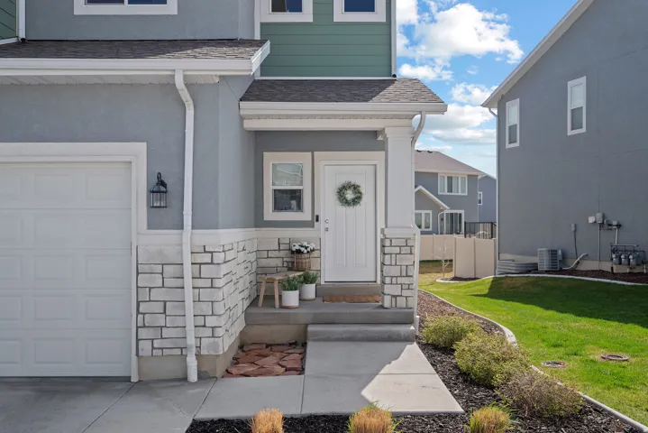Entrance to property with stone siding, roof with shingles, stucco siding, a lawn, and a garage