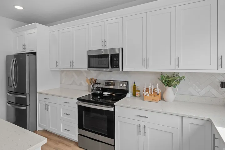 Kitchen featuring stainless steel appliances, light stone countertops, white cabinets, light wood-type flooring, and backsplash