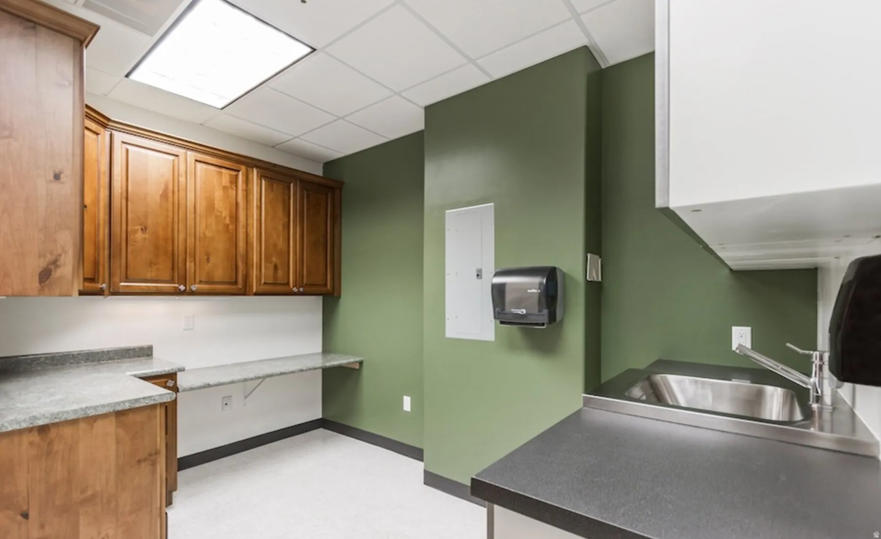 Kitchen with a drop ceiling, wood finish cabinets, electric panel, light colored carpet, and dark countertops