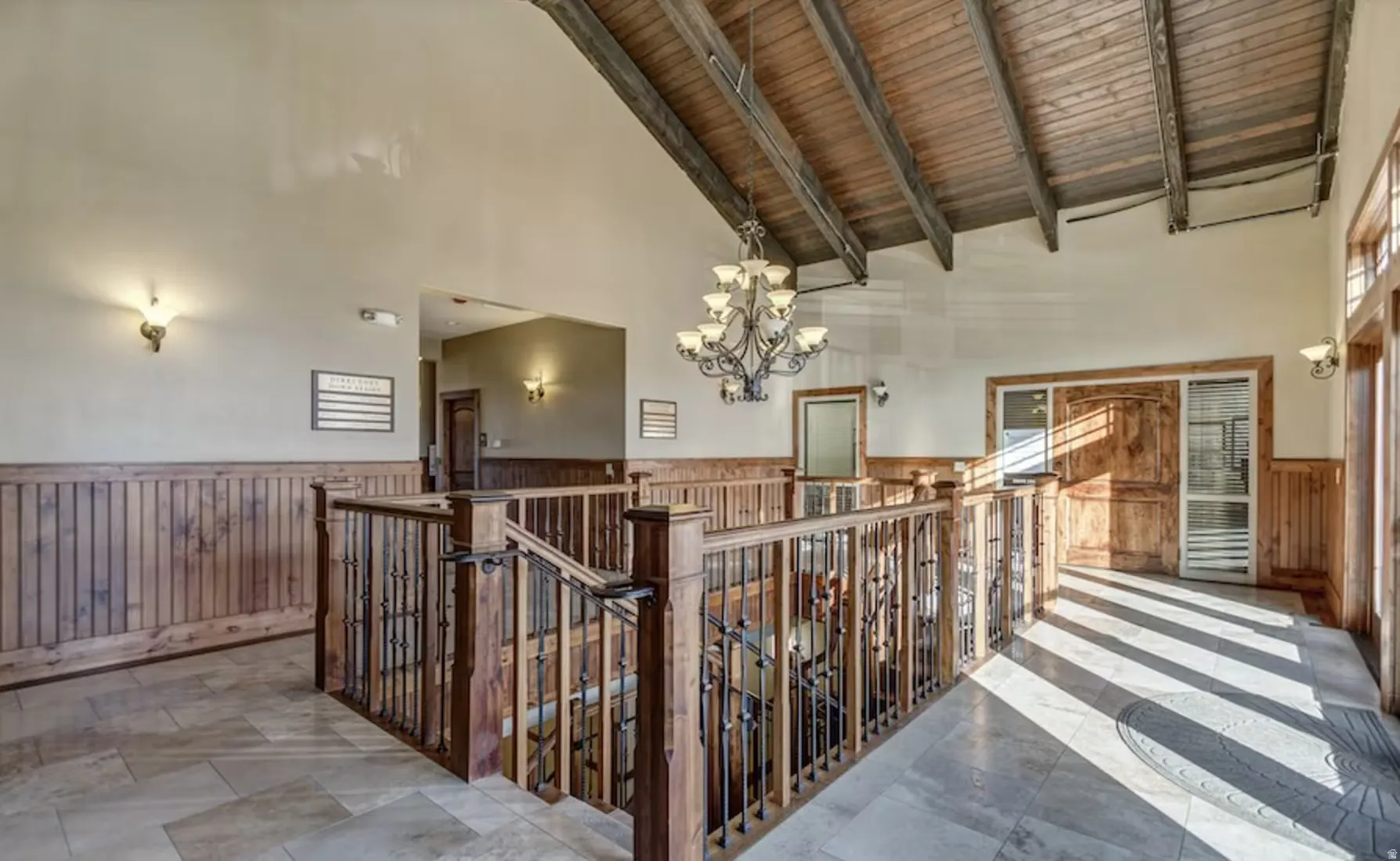 Hall with hanging lights, a wainscoted wall, a high wood beamed ceiling, wooden walls, and an upstairs landing