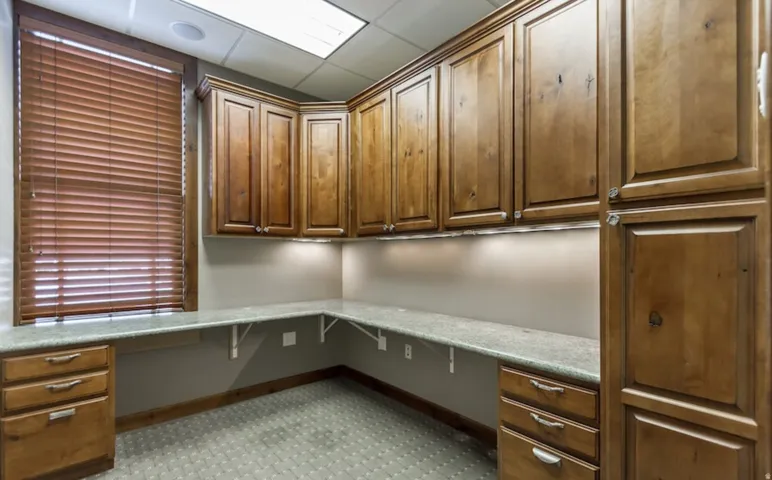 Unfurnished office with built in desk, a paneled ceiling, and light carpet
