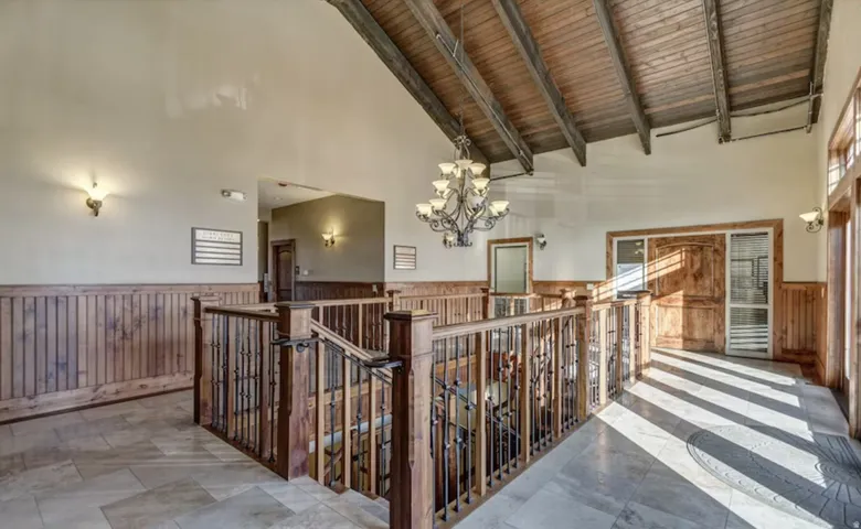Hall with hanging lights, a wainscoted wall, a high wood beamed ceiling, wooden walls, and an upstairs landing
