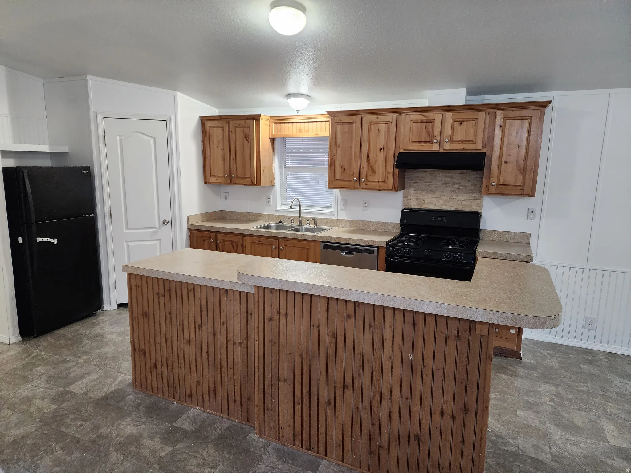 Kitchen featuring black appliances, a kitchen island, light countertops, wood finish cabinets, and stone finish floors
