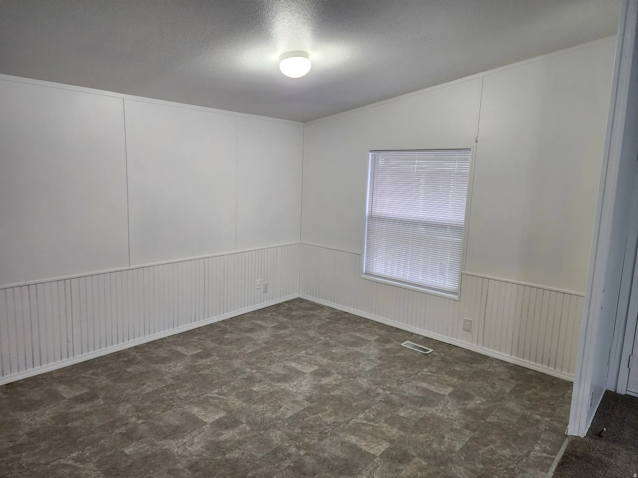 Spare room with a decorative wall, a textured ceiling, dark flooring, and wainscoting