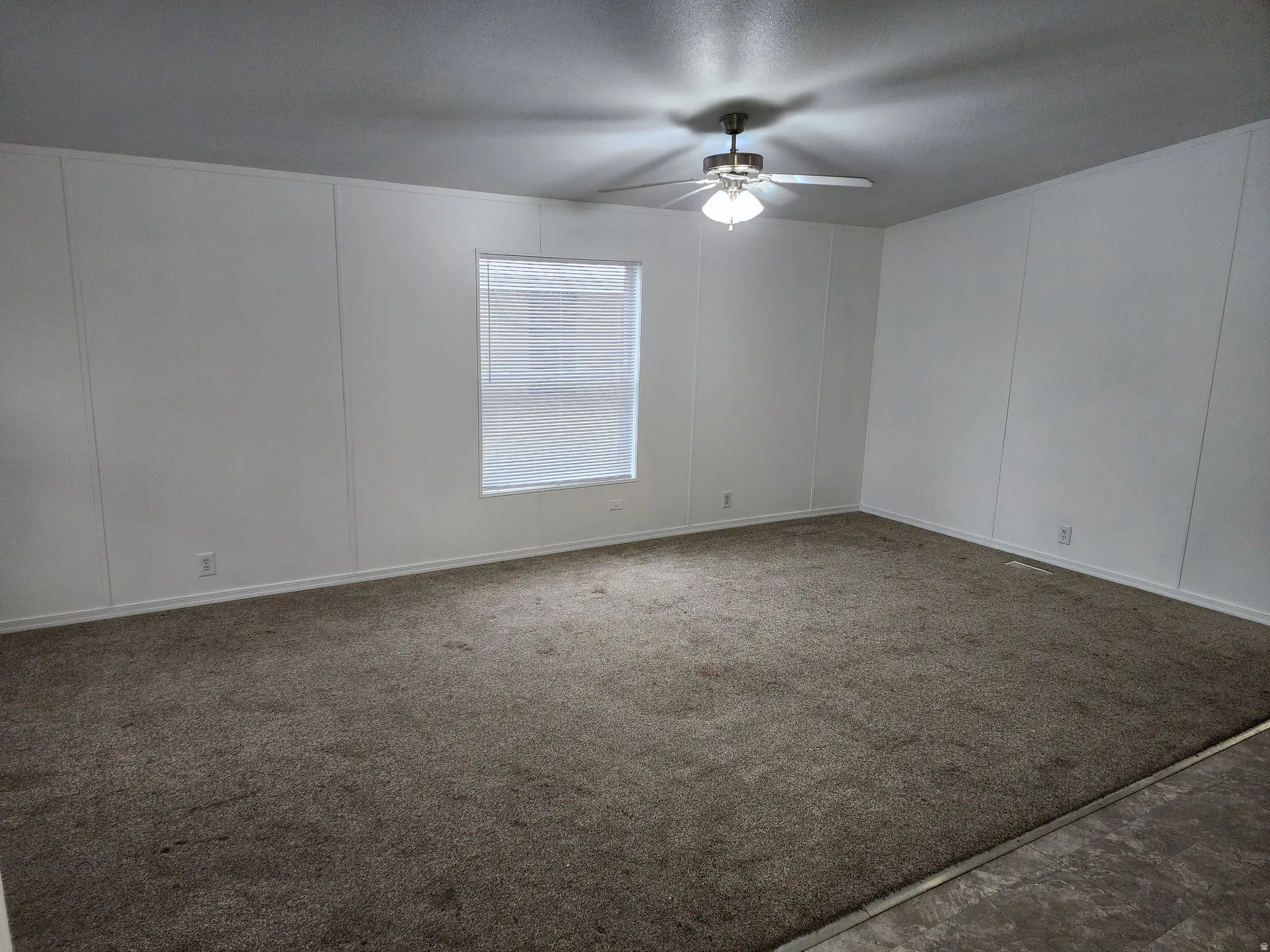 Spare room with a decorative wall, a ceiling fan, and dark carpet