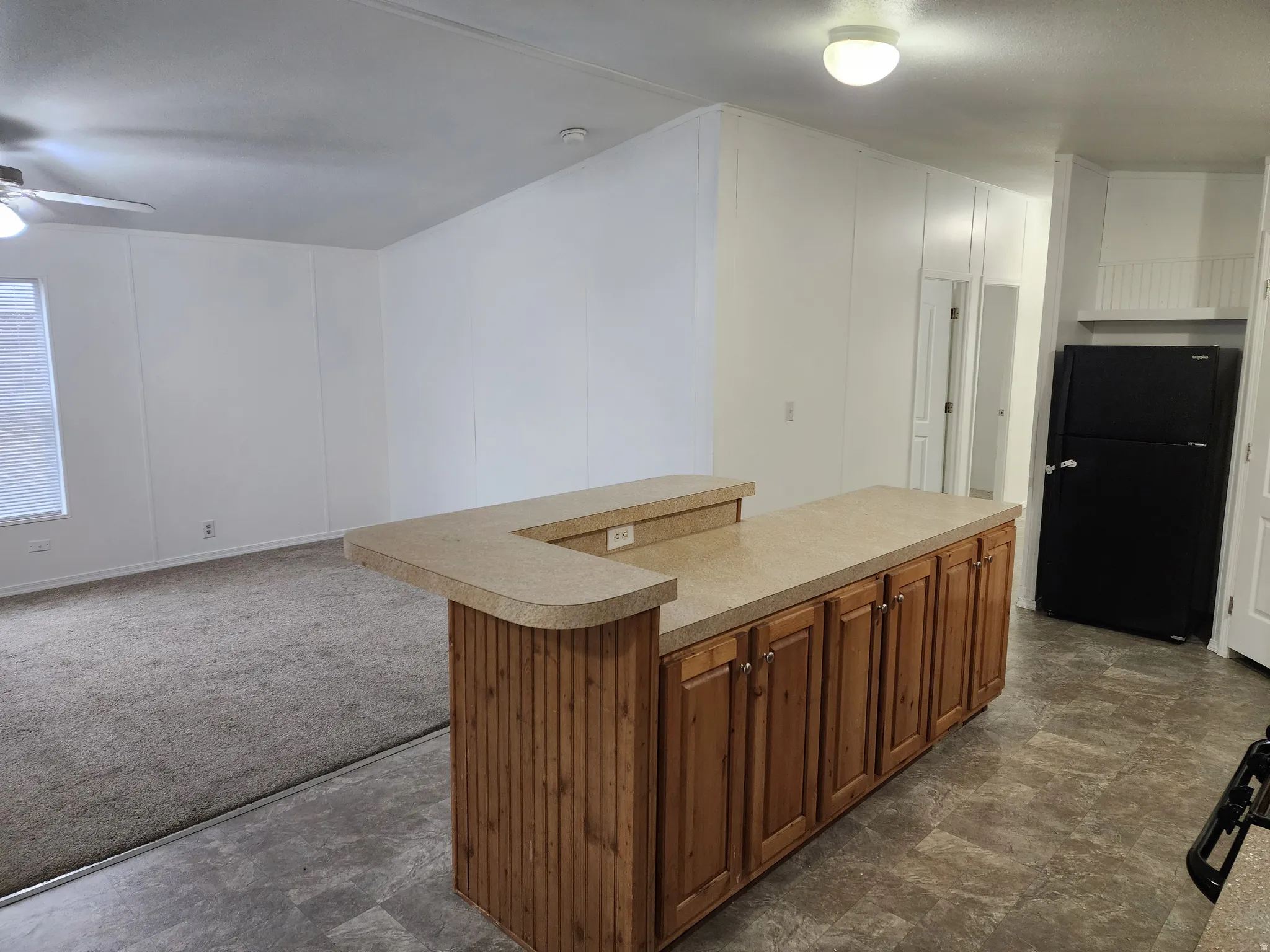 Kitchen with freestanding refrigerator, wood finish cabinetry, open floor plan, a kitchen island, and light countertops