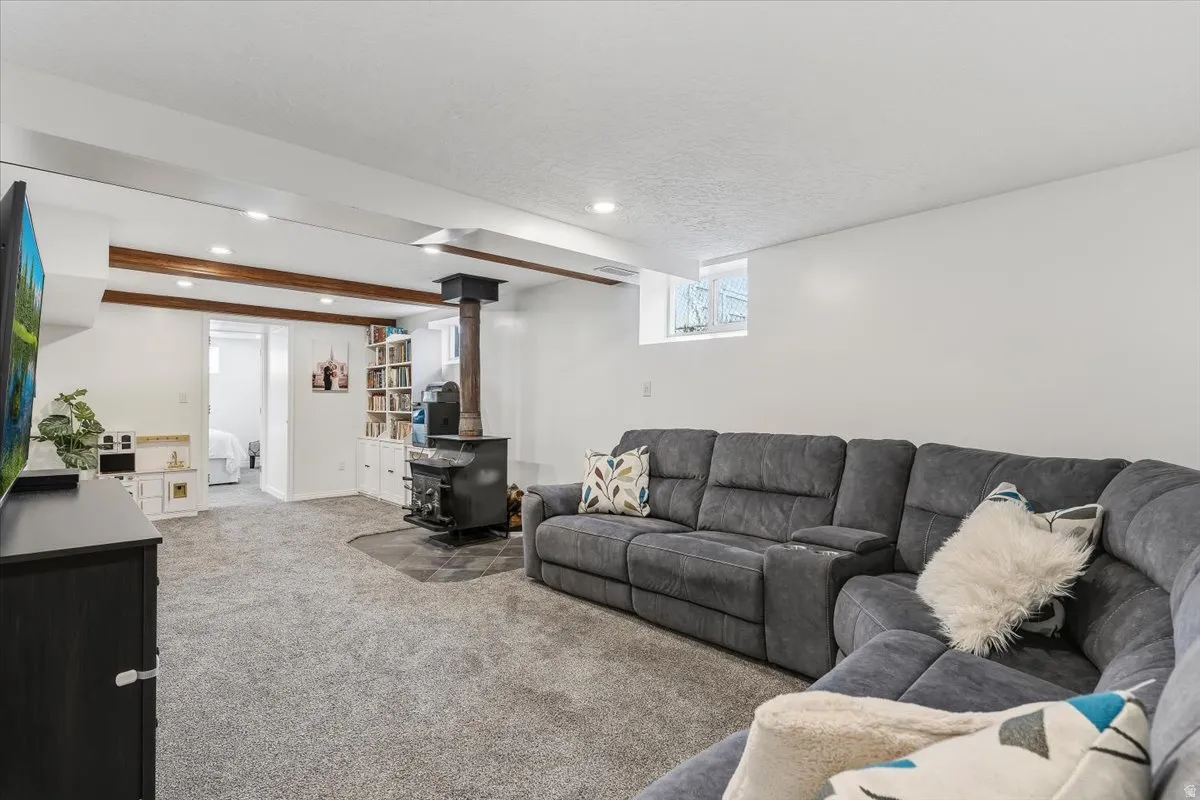 Living room with carpet floors, a wood stove, recessed lighting, a textured ceiling, and beam ceiling