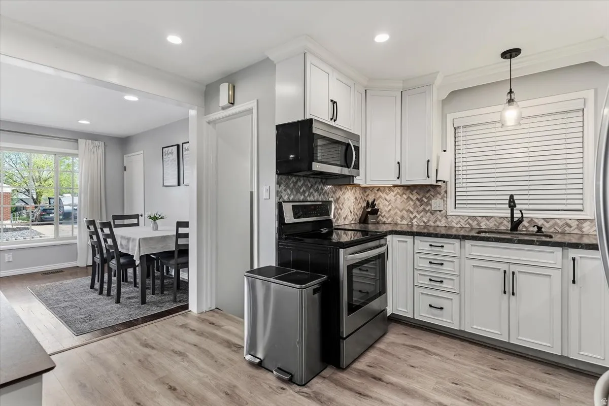 Kitchen featuring stainless steel appliances, backsplash, white cabinetry, light wood-type flooring, and decorative light fixtures