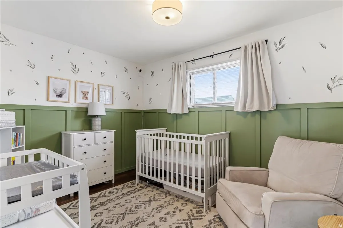 Bedroom with a decorative wall, wainscoting, a crib, and light wood-type flooring