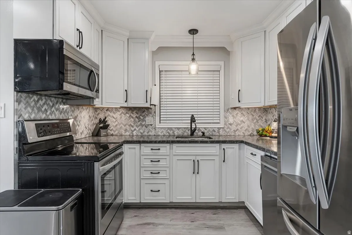 Kitchen with stainless steel appliances, white cabinetry, pendant lighting, and backsplash