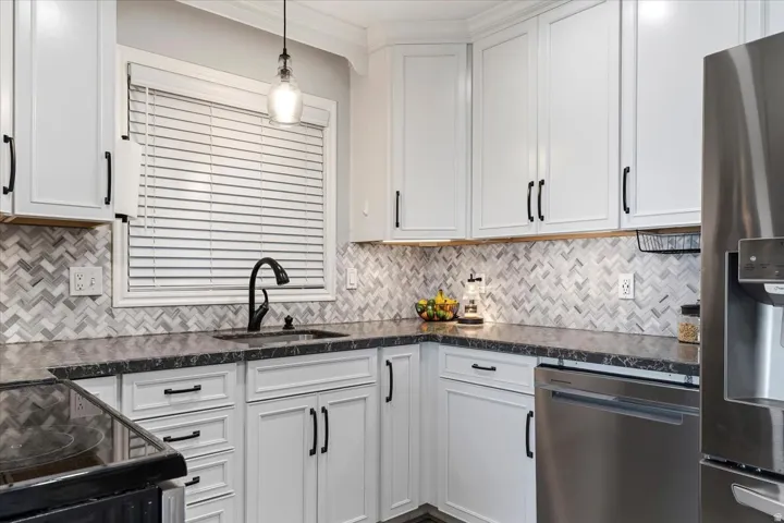 Kitchen featuring stainless steel appliances, white cabinetry, dark stone counters, decorative light fixtures, and backsplash