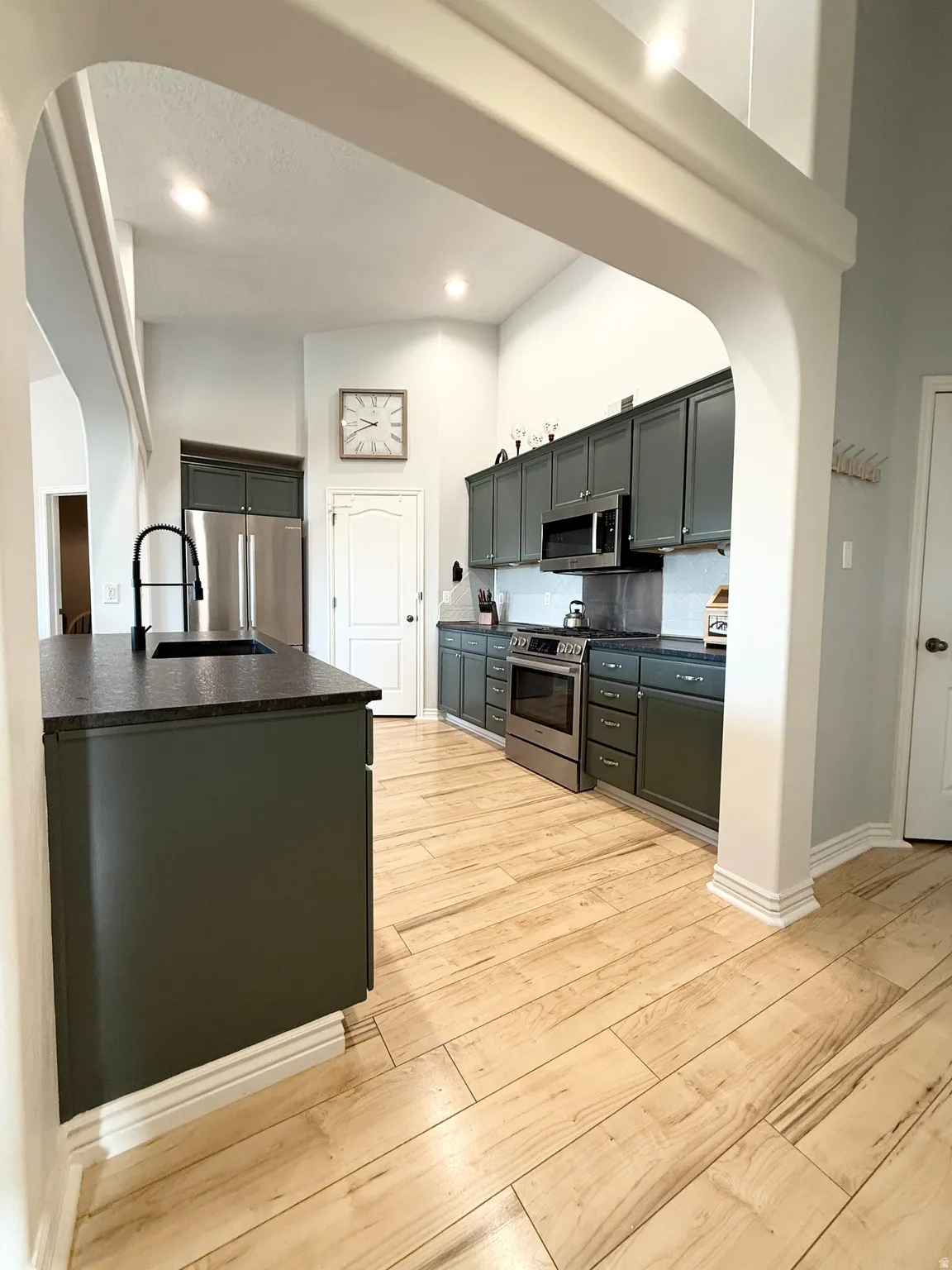 Kitchen featuring arched walkways, light wood-style floors, stainless steel appliances, dark countertops, and a high ceiling