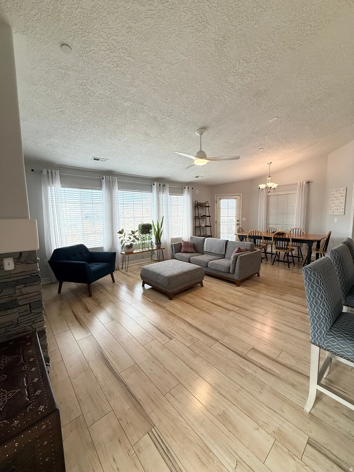Living room featuring a ceiling fan, a textured ceiling, light wood finished floors, and suspended lighting