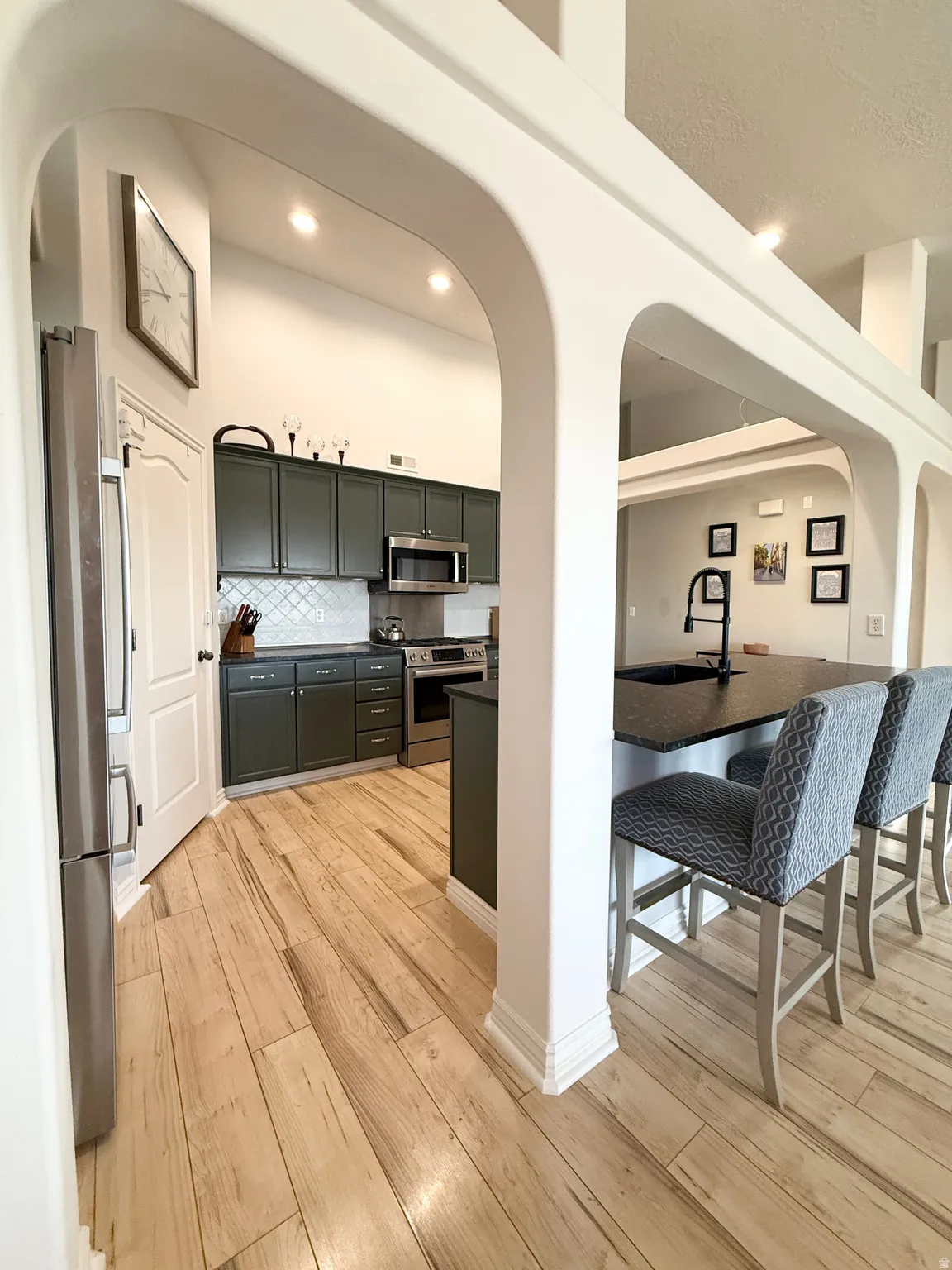 Kitchen featuring arched walkways, stainless steel appliances, light wood-style flooring, and recessed lighting